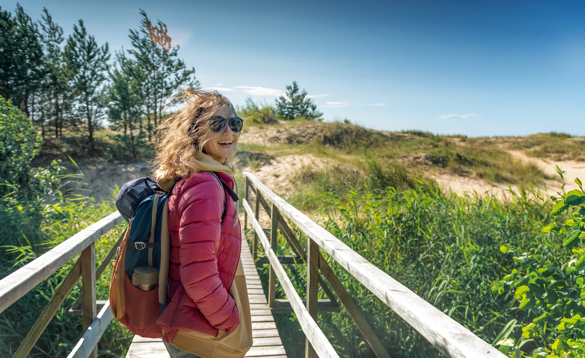 Молодая счастливая красивая девушка гуляет по холодному берегу Балтийского моря в ветреную солнечную погоду.