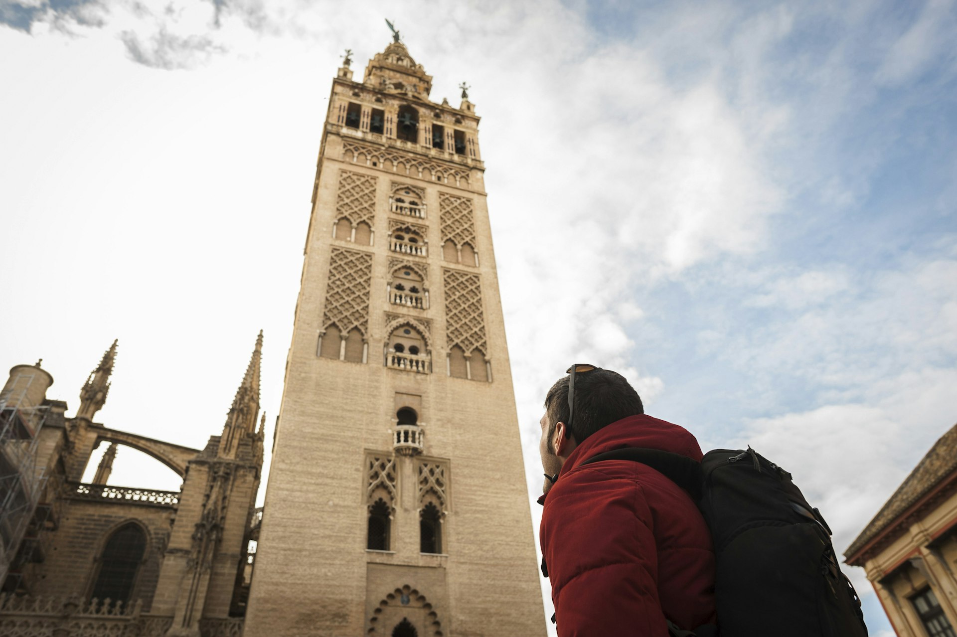 Низкий угол обзора туриста, смотрящего на Ла-Хиральду в Севильском соборе на фоне облачного неба в городе
